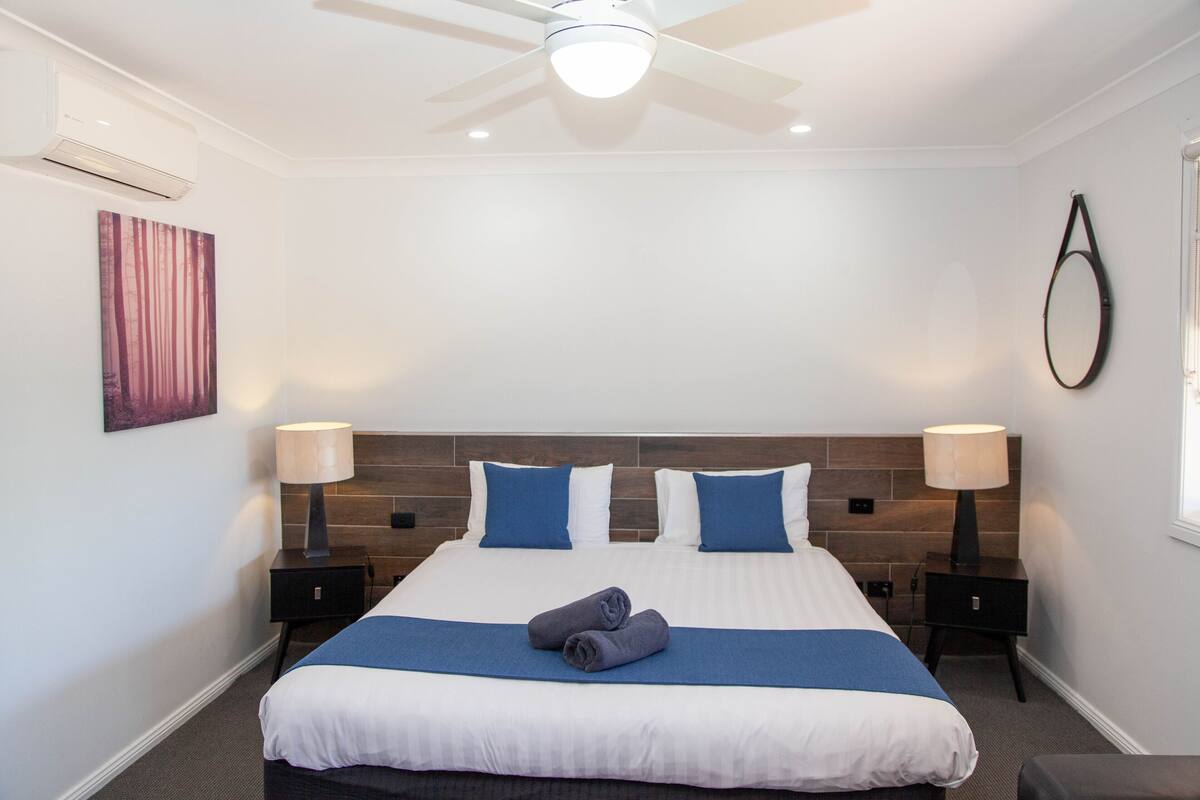 A hotel room with a large bed, two bedside tables, a ceiling fan, and a wall-mounted mirror.