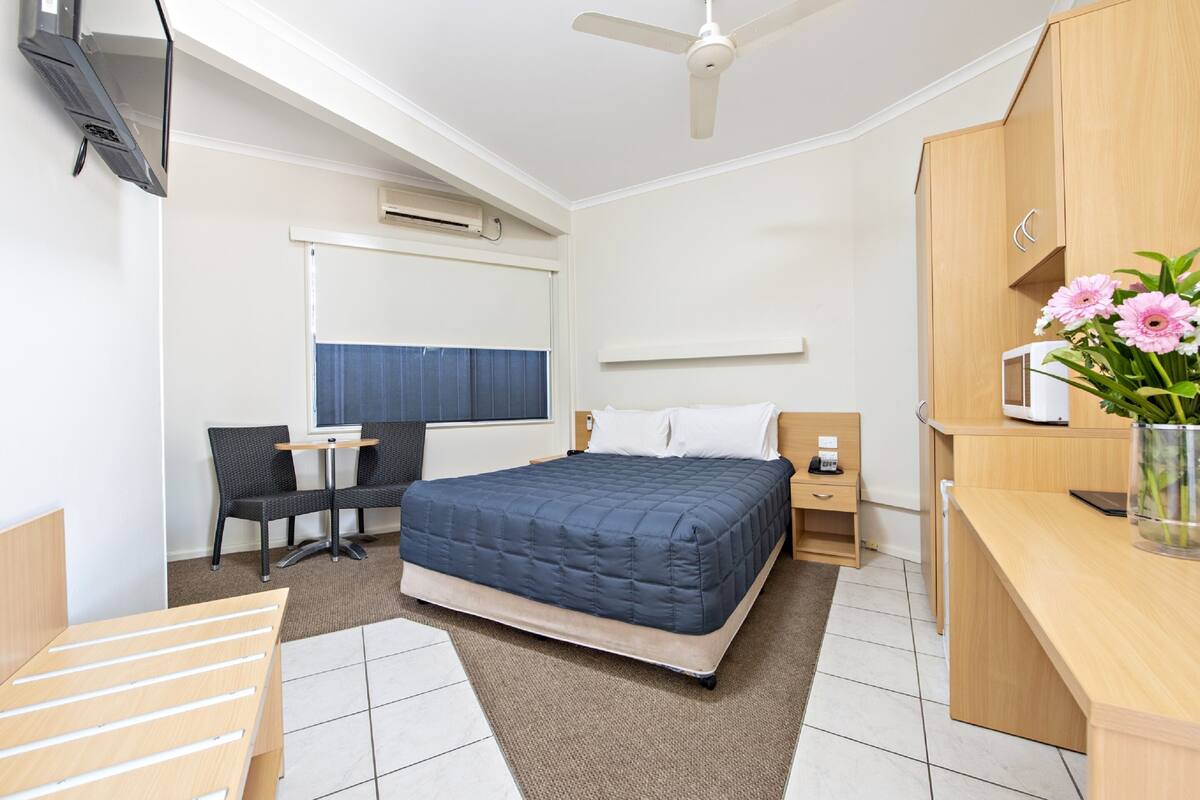 A modern hotel room with a bed, a desk, a chair, a TV, and a ceiling fan.