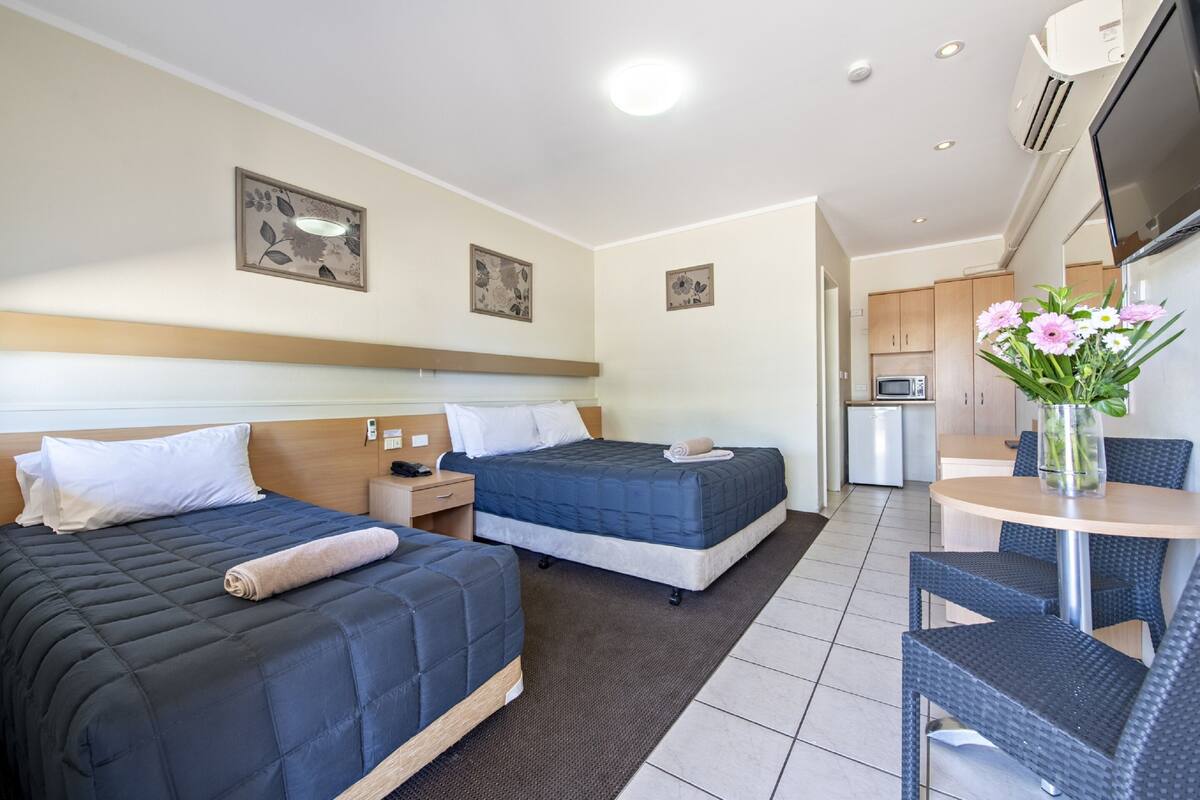 A hotel room with two beds, a small kitchenette, a dining area, and a TV.