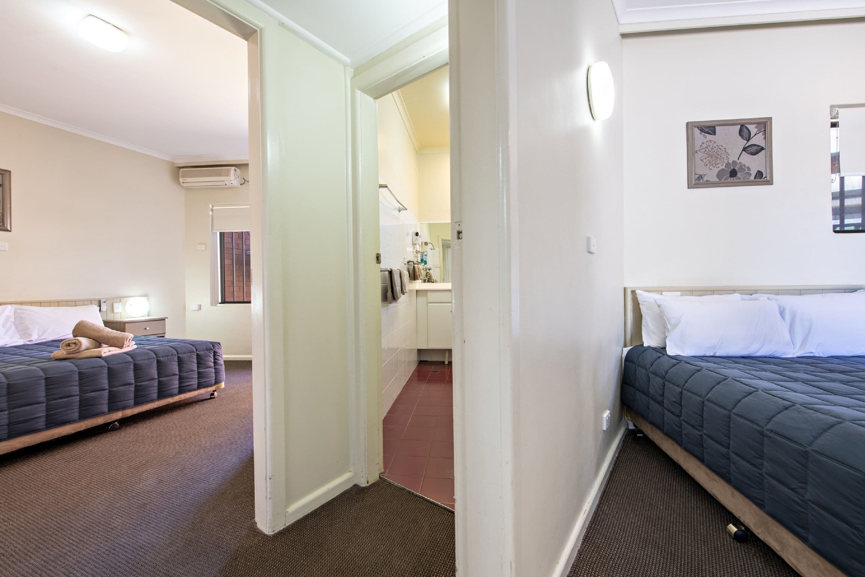 Una habitación de hotel con dos camas, un baño y un pasillo.