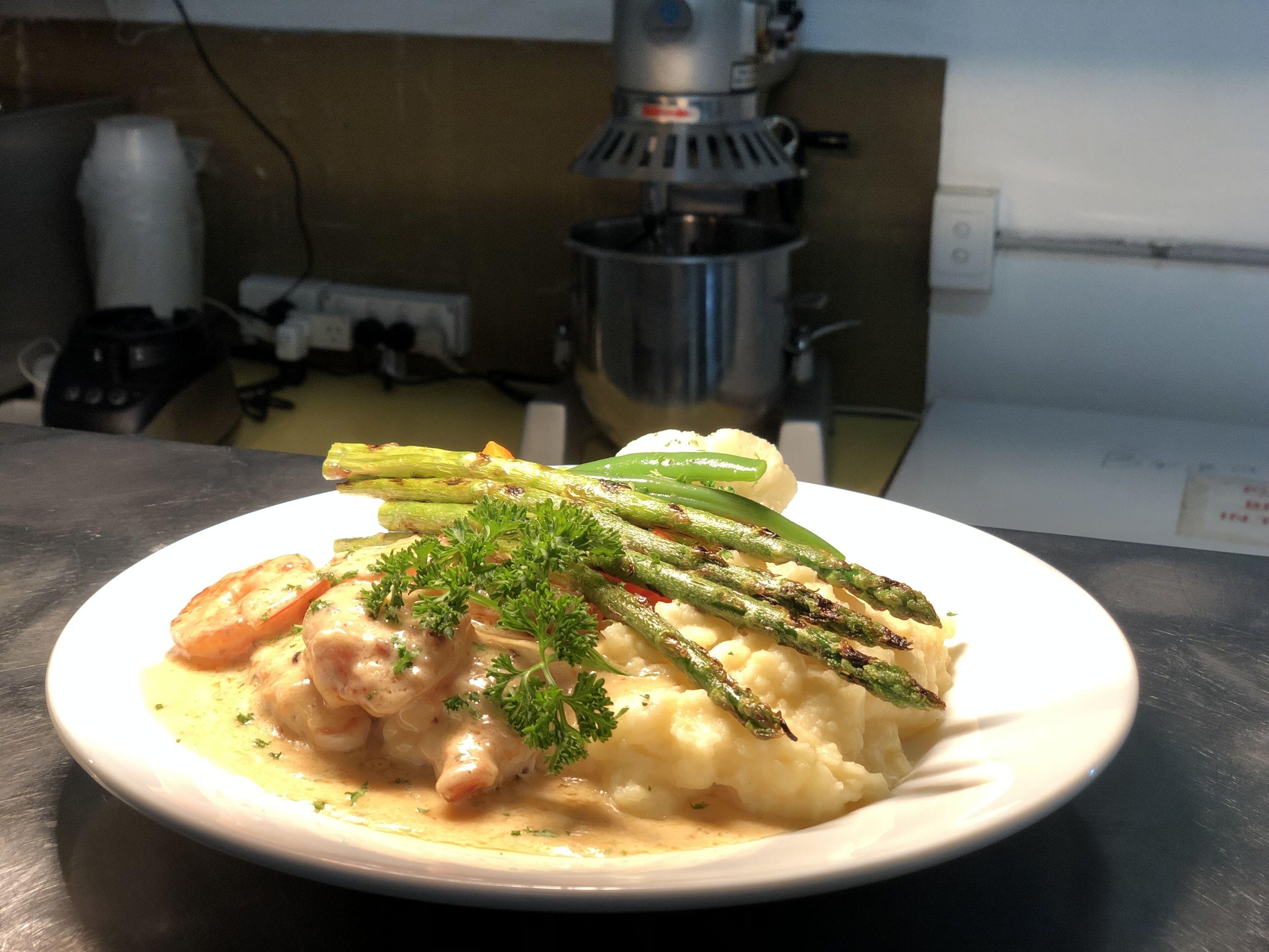 Un piatto di cibo con asparagi, patate e salsa cremosa, servito su un piatto bianco.