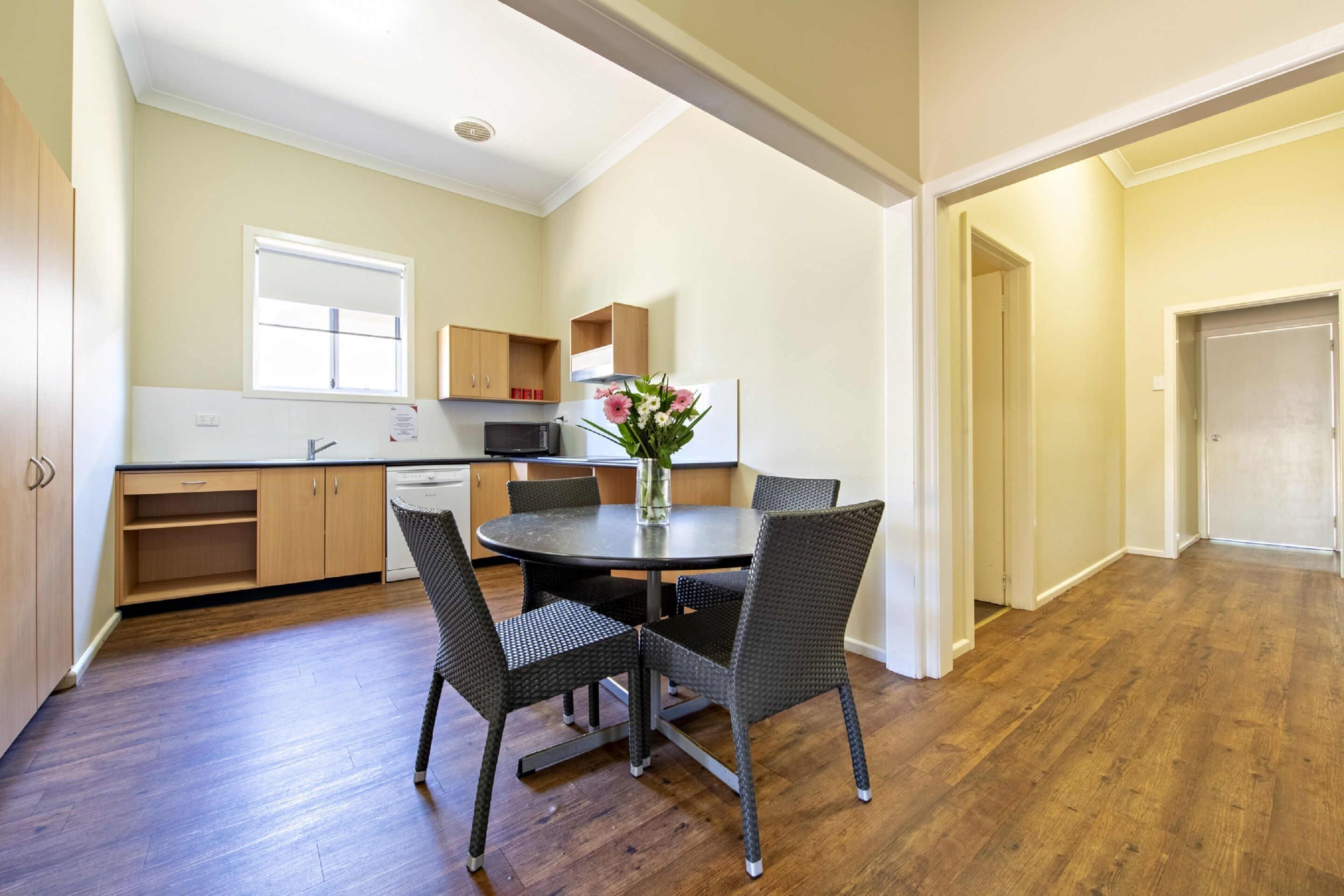 A modern kitchen with wooden cabinets, a dining table with chairs, and a vase with flowers.