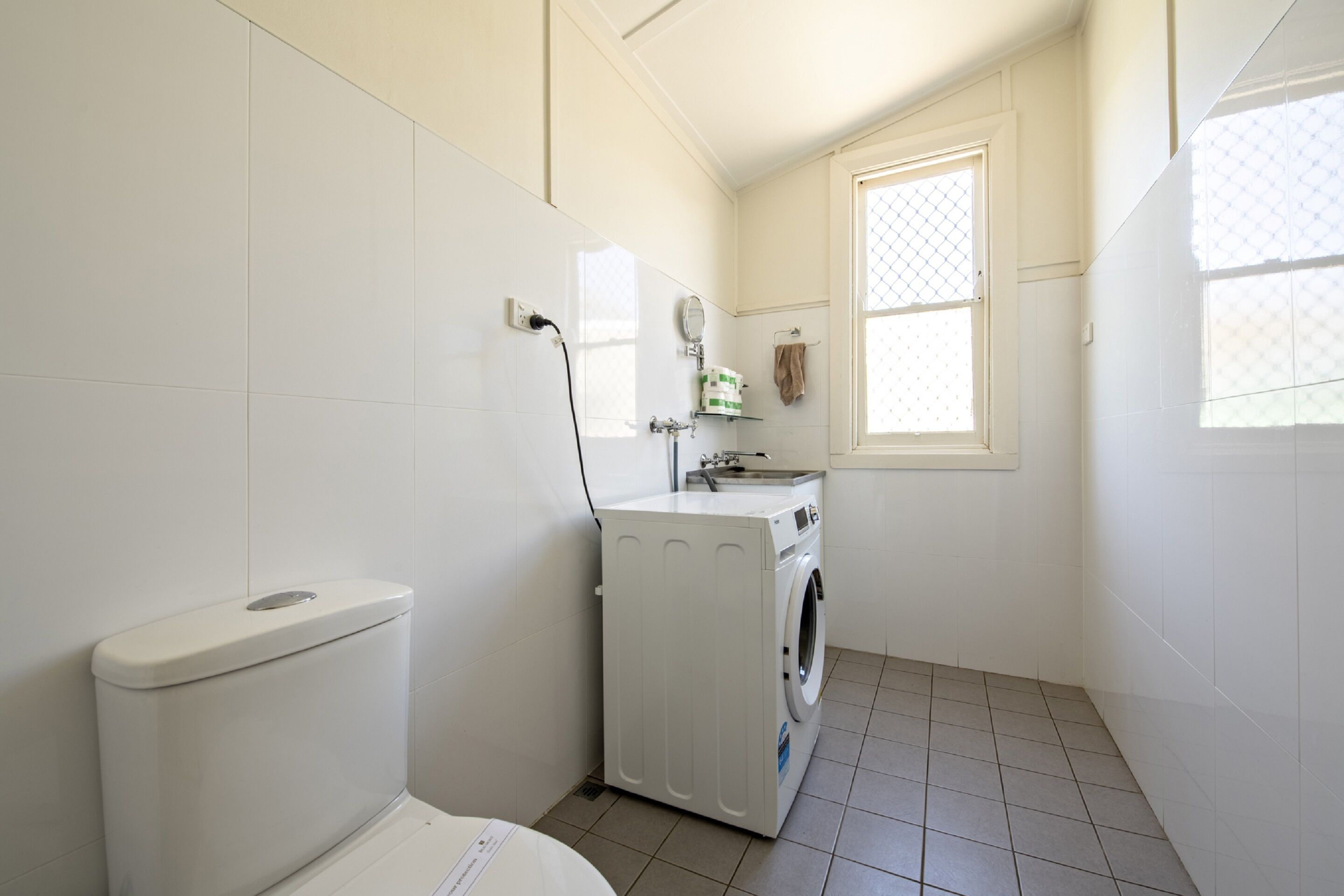 Une petite salle de bain comprenant des toilettes, un lave-linge et une petite fenêtre.