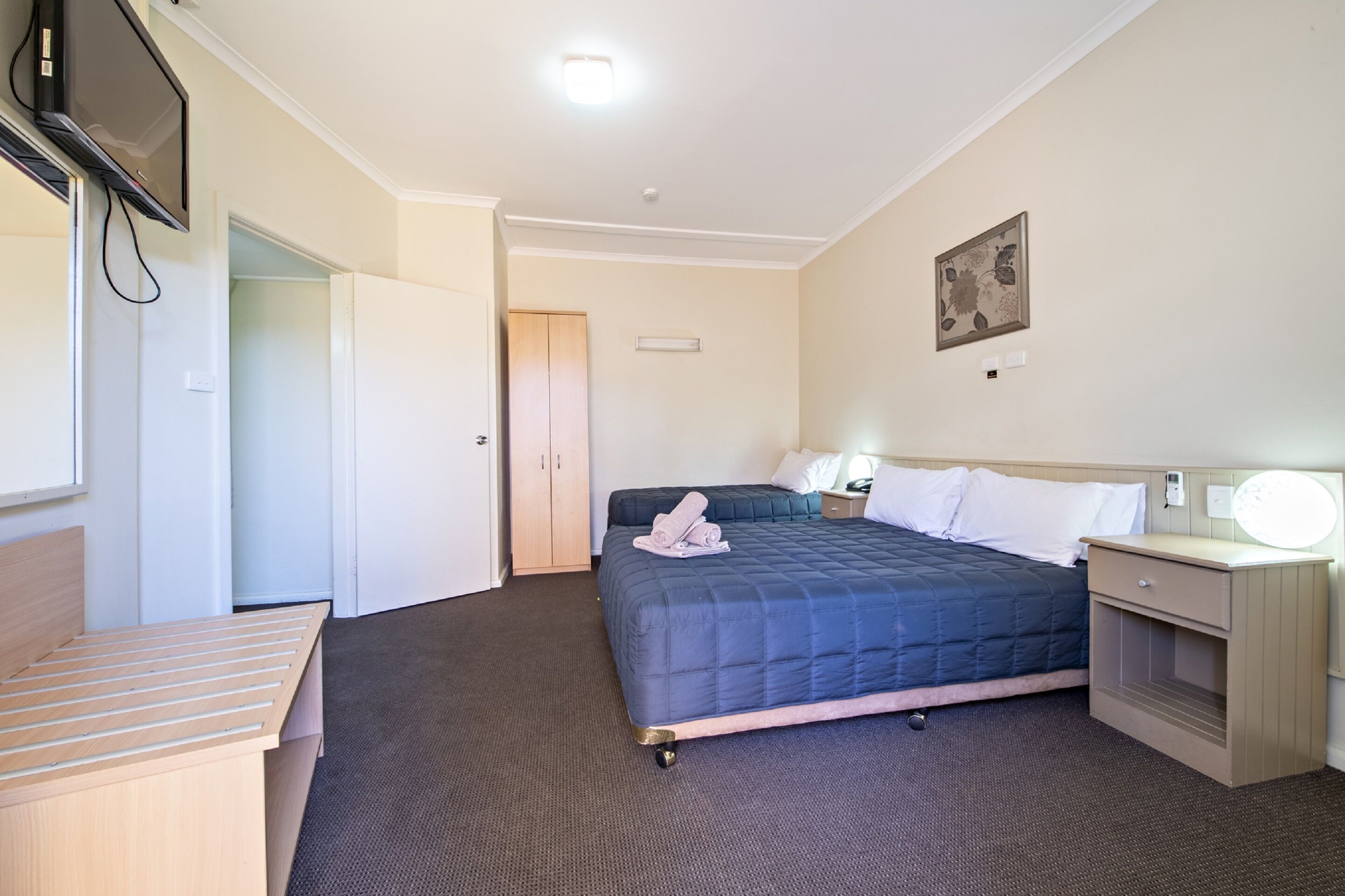 A hotel room with a bed, bedside tables, a desk, and a TV mounted on the wall.