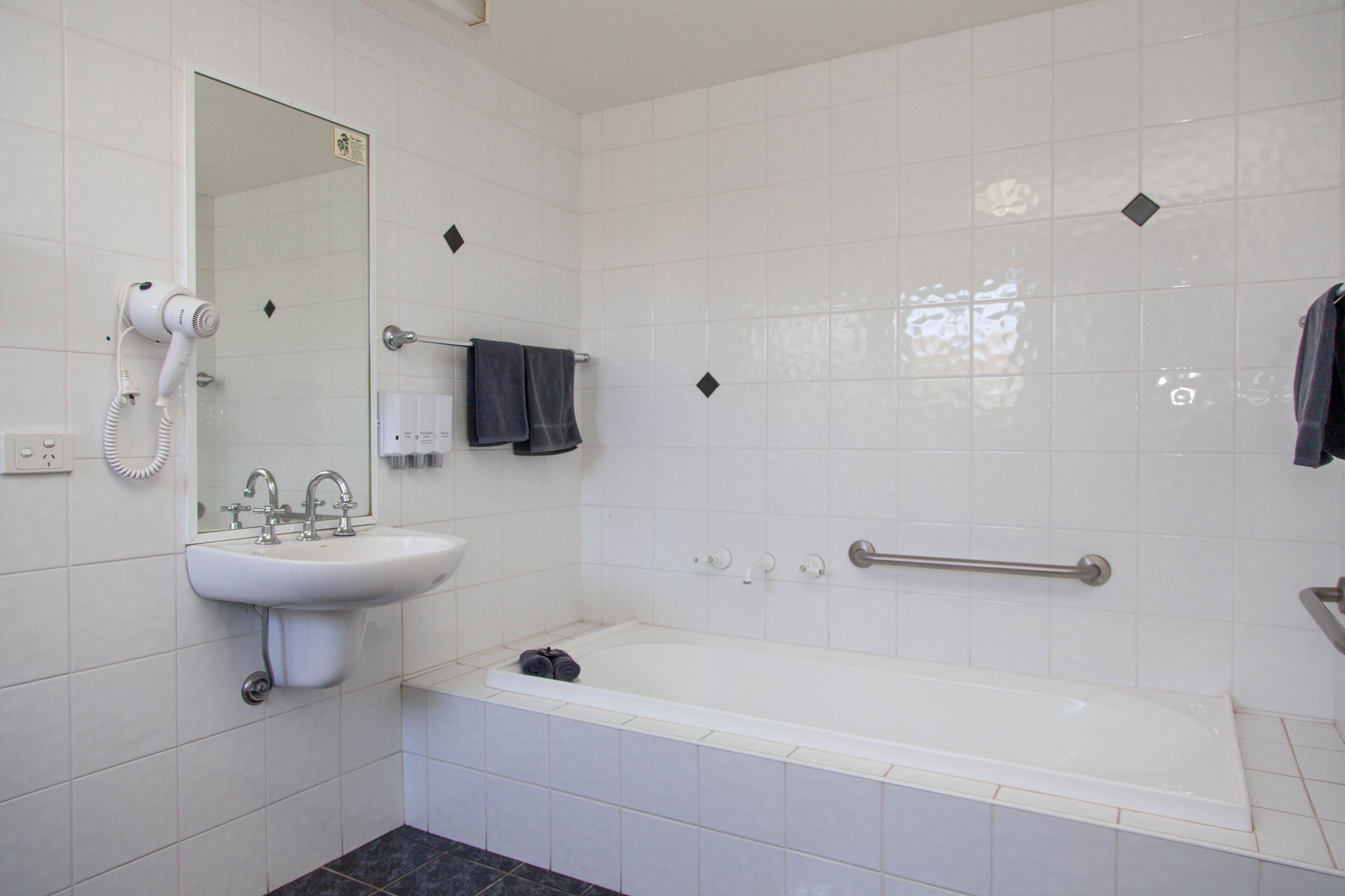 Een badkamer met een wastafel, spiegel, haardroger en bad.