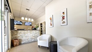 A reception area with a stone wall, two white armchairs, a black ottoman, and a counter with a computer and a vase of flowers. - Matilda Motor Inn (Dubbo)