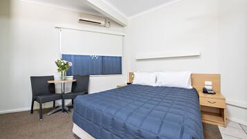 Habitación de hotel con una cama grande, un escritorio con una silla, una mesita con un florero y una ventana con persianas.