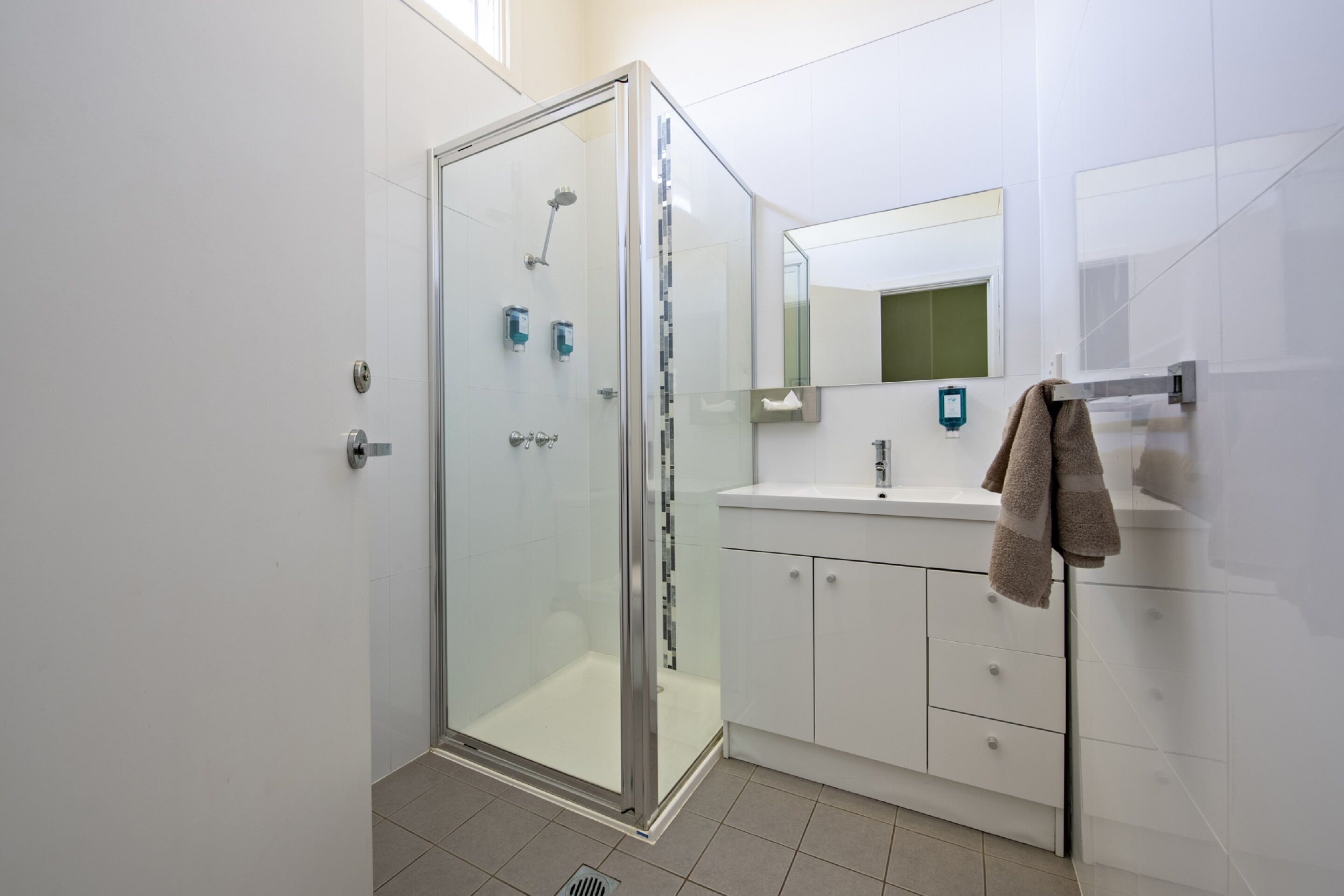 Un baño moderno con cabina de ducha de vidrio, un lavabo blanco y un perchero para toallas.