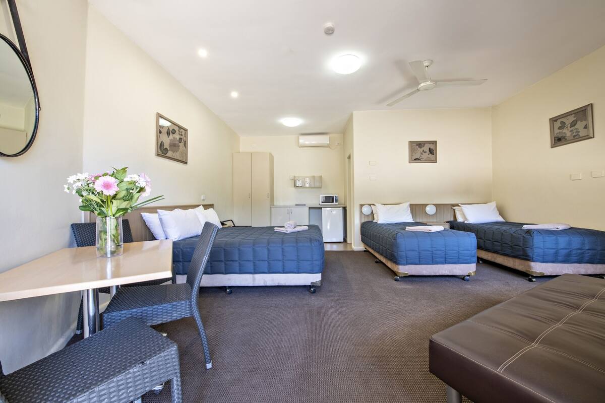 A hotel room with two beds, a desk, a chair, a small table, and a vase with flowers.