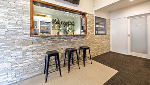 A bar area with a stone wall, a TV mounted above the bar, and three black stools. - Matilda Motor Inn (Dubbo)