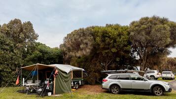 A camping site with a tent, a small table, chairs, and a vehicle parked nearby.