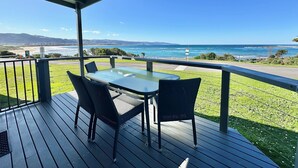 Un espacio exterior techado con una mesa y sillas, con vistas a un paisaje costero con colinas y una playa.