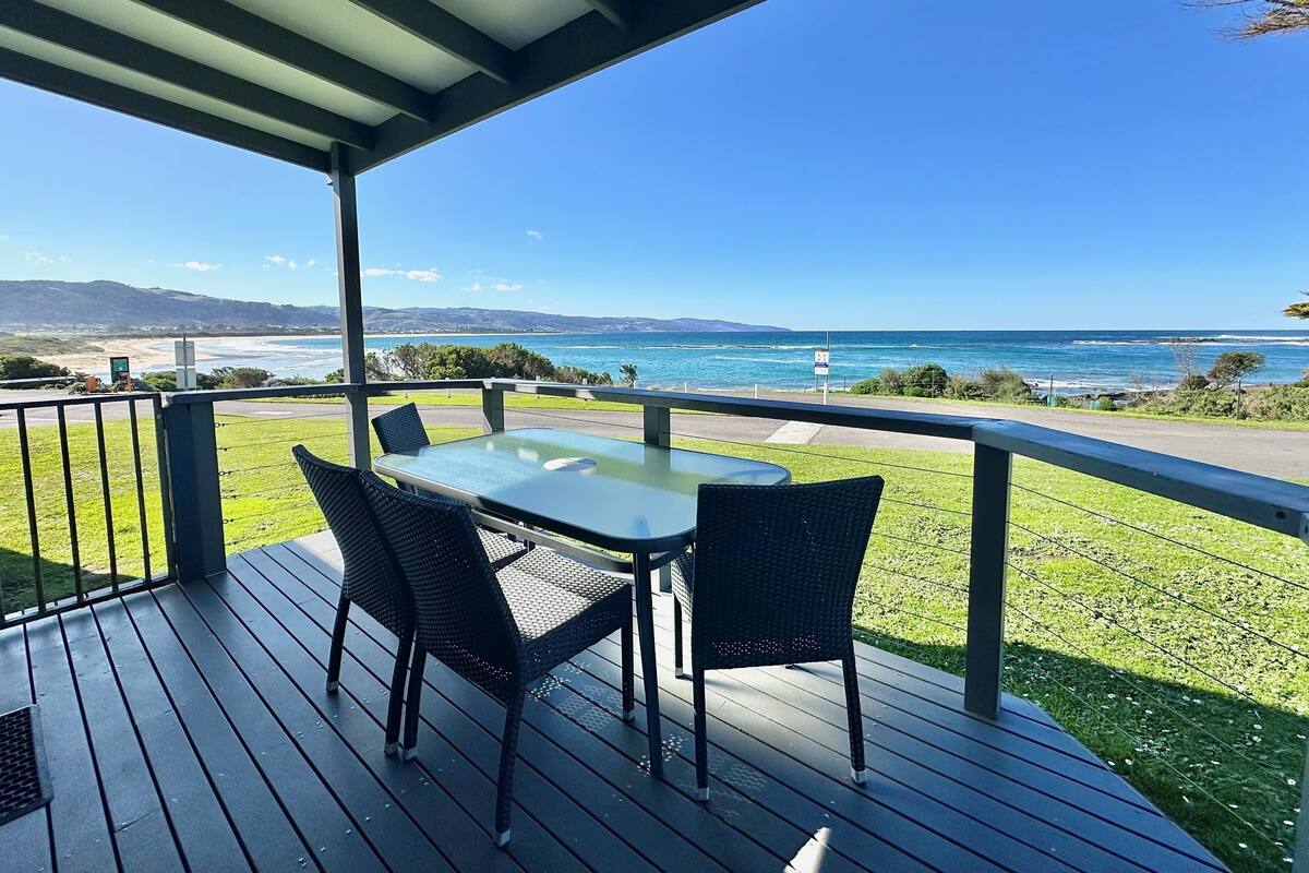 Un espacio exterior techado con una mesa y sillas, con vistas a un paisaje costero con colinas y una playa.