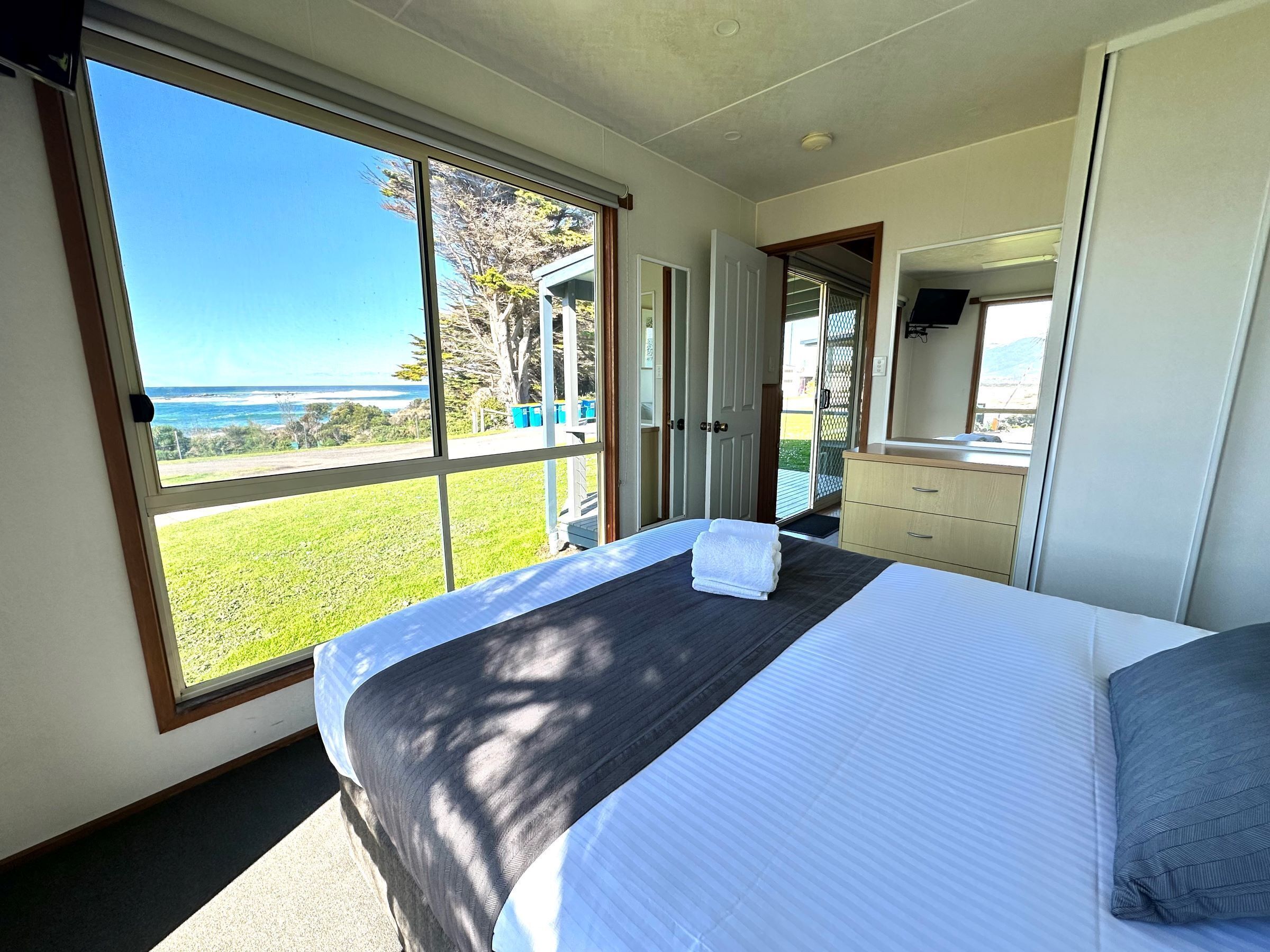 A bedroom with a large window, a bed, a dresser, and a mirror.