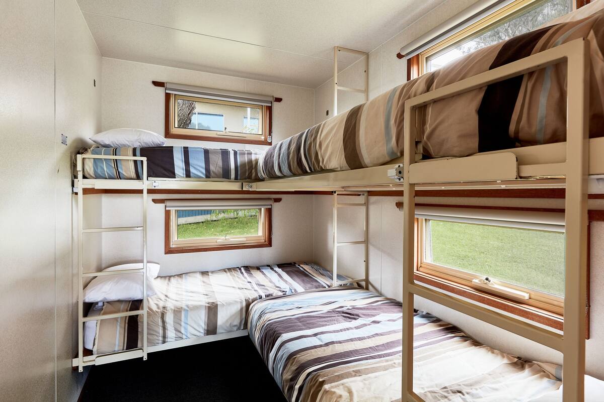 Habitación con literas, dos ventanas, una escalera y un estante pequeño.