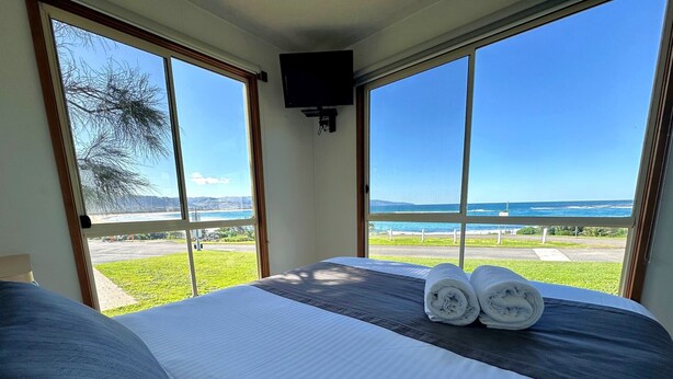 Habitación de hotel con una cama, dos ventanas y vista al océano.