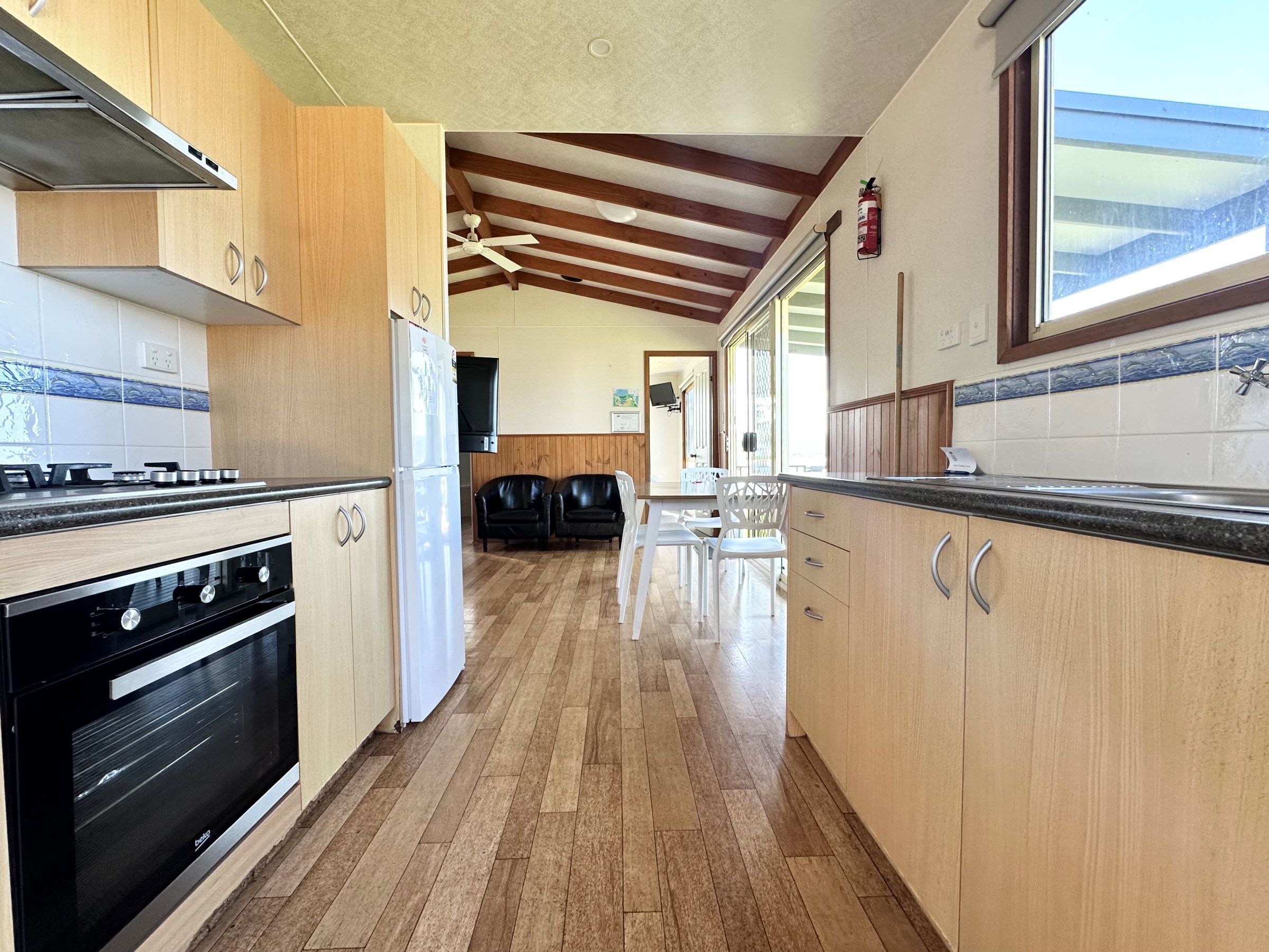 A kitchen with wooden cabinets, a stove, and a refrigerator. There is a dining area with chairs and a table.