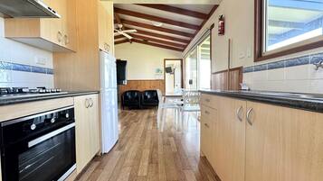 A kitchen with wooden cabinets, a stove, and a refrigerator. There is a dining area with chairs and a table.