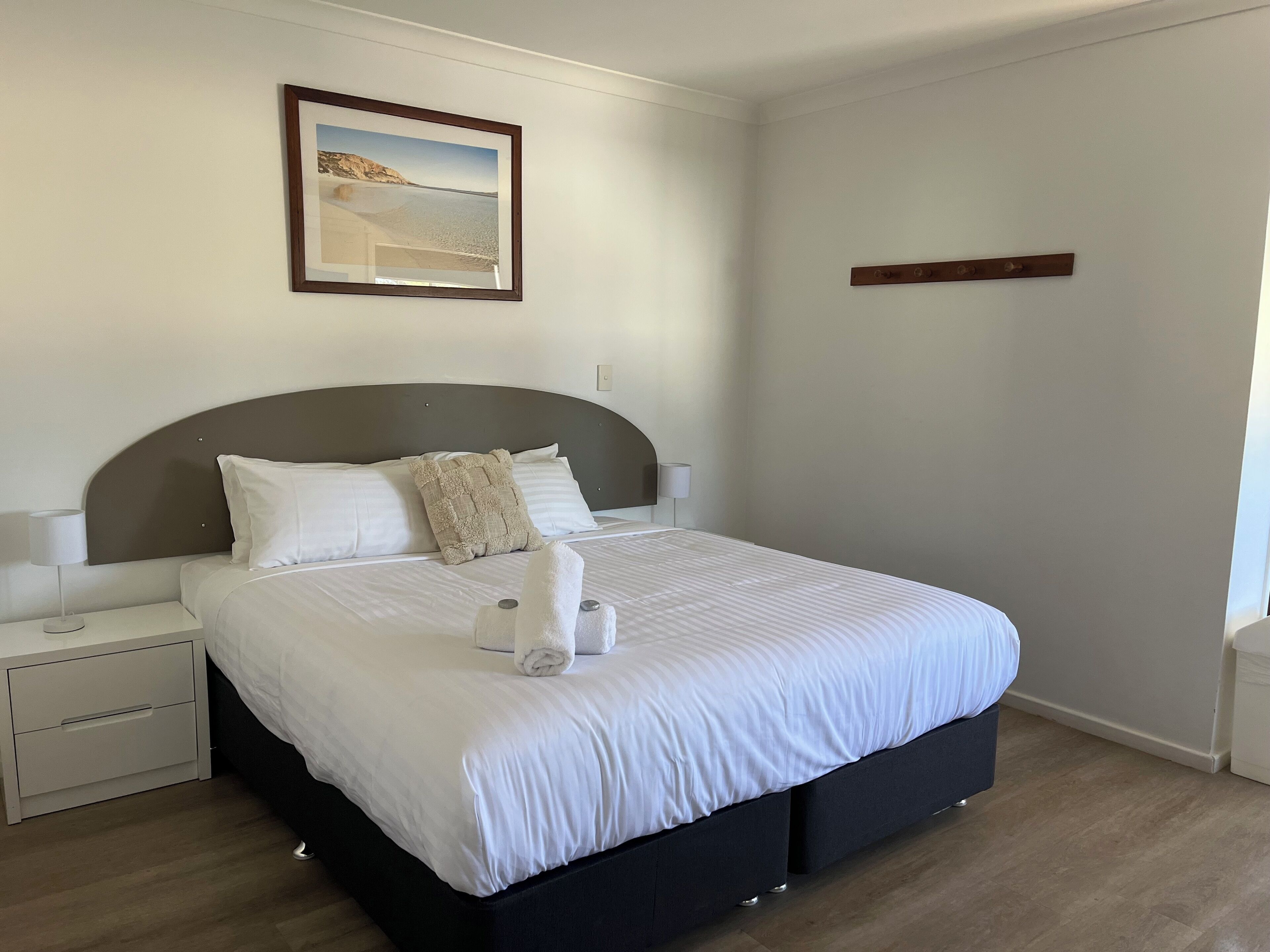 A neatly made bed with white linens, a headboard, and a bedside table with a lamp.