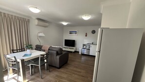 A compact living space with a dining area, a sofa, a TV, a kitchenette, and a refrigerator. - Clearwater Motel Apartments (Esperance)