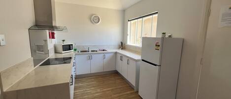 Eine moderne Küche mit weißen Schränken, einer Mikrowelle, einem Kühlschrank und einem Fenster, das natürliches Licht hereinlässt.