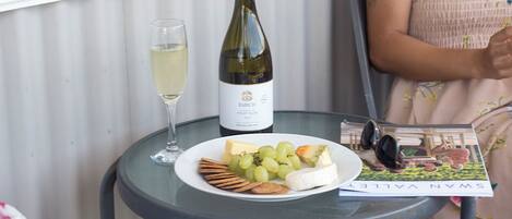 A table with a bottle of wine, a glass, a plate with grapes, cheese, and crackers, and a magazine.