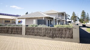A two-story building with a balcony, a garage, and a landscaped area with shrubs. - Clearwater Motel Apartments (Esperance)