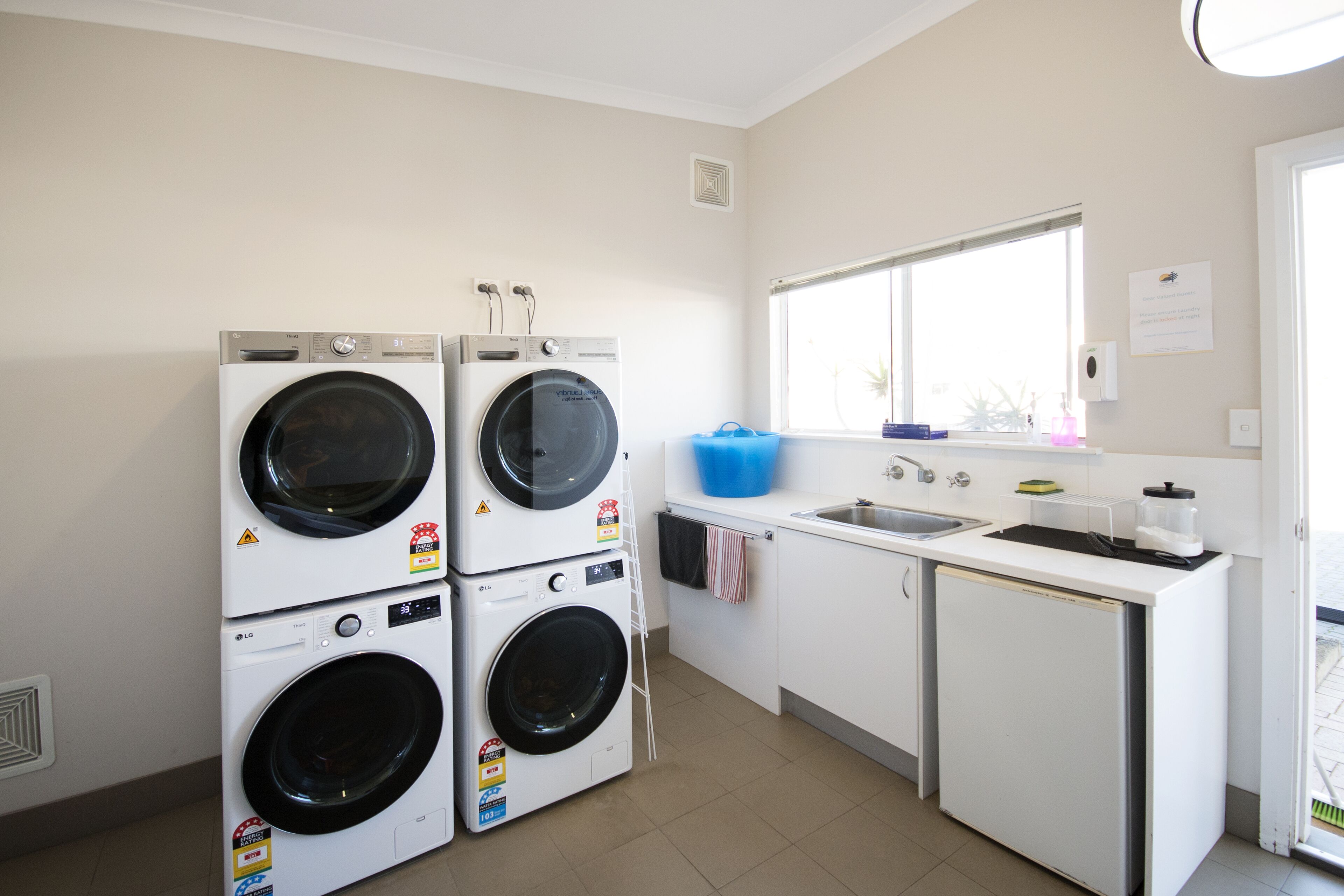 A laundry room with two stacked front-loading washing machines, a sink, and a small refrigerator.