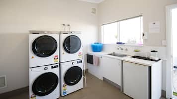 A laundry room with two stacked front-loading washing machines, a sink, and a small refrigerator.