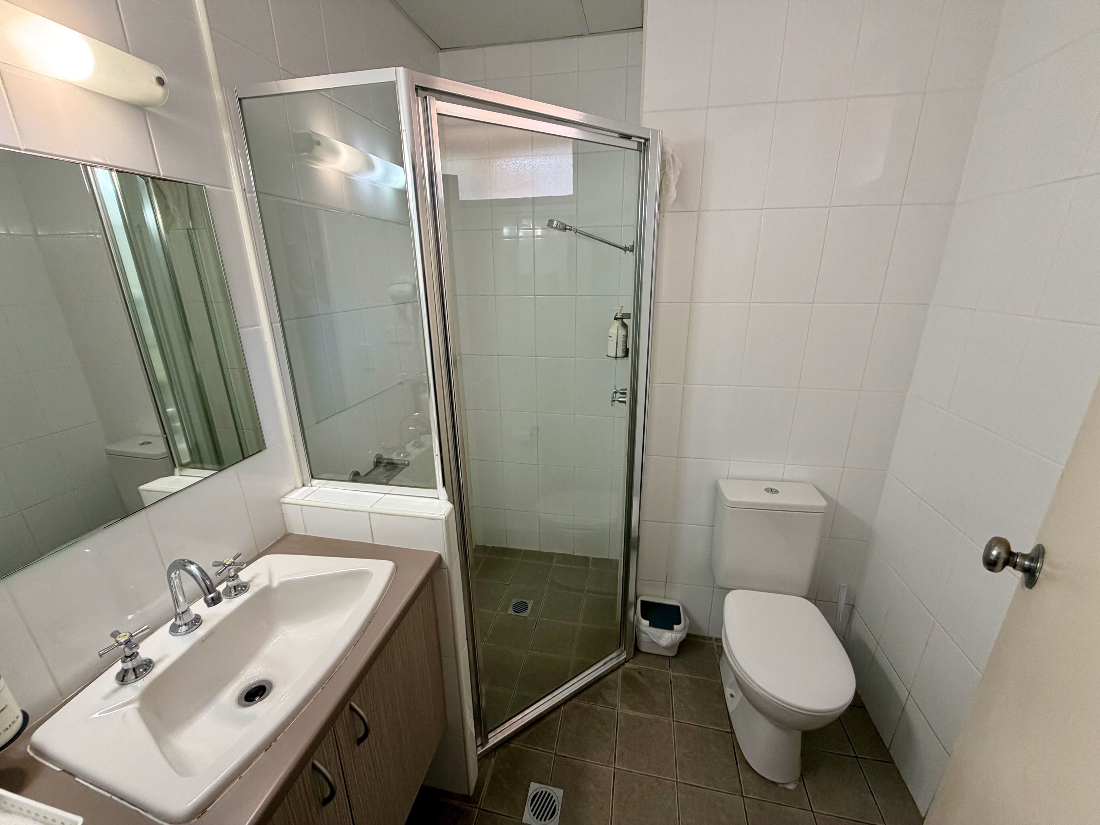 A bathroom with a glass-enclosed shower, a white sink with a mirror, and a toilet.