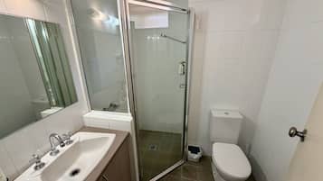 Un baño con ducha de vidrio, un lavamanos blanco con espejo y un inodoro.