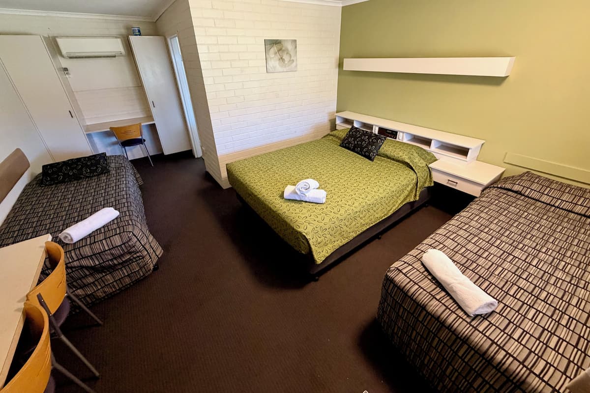 Una habitación con dos camas individuales, una cama doble, una silla, un escritorio y un armario.