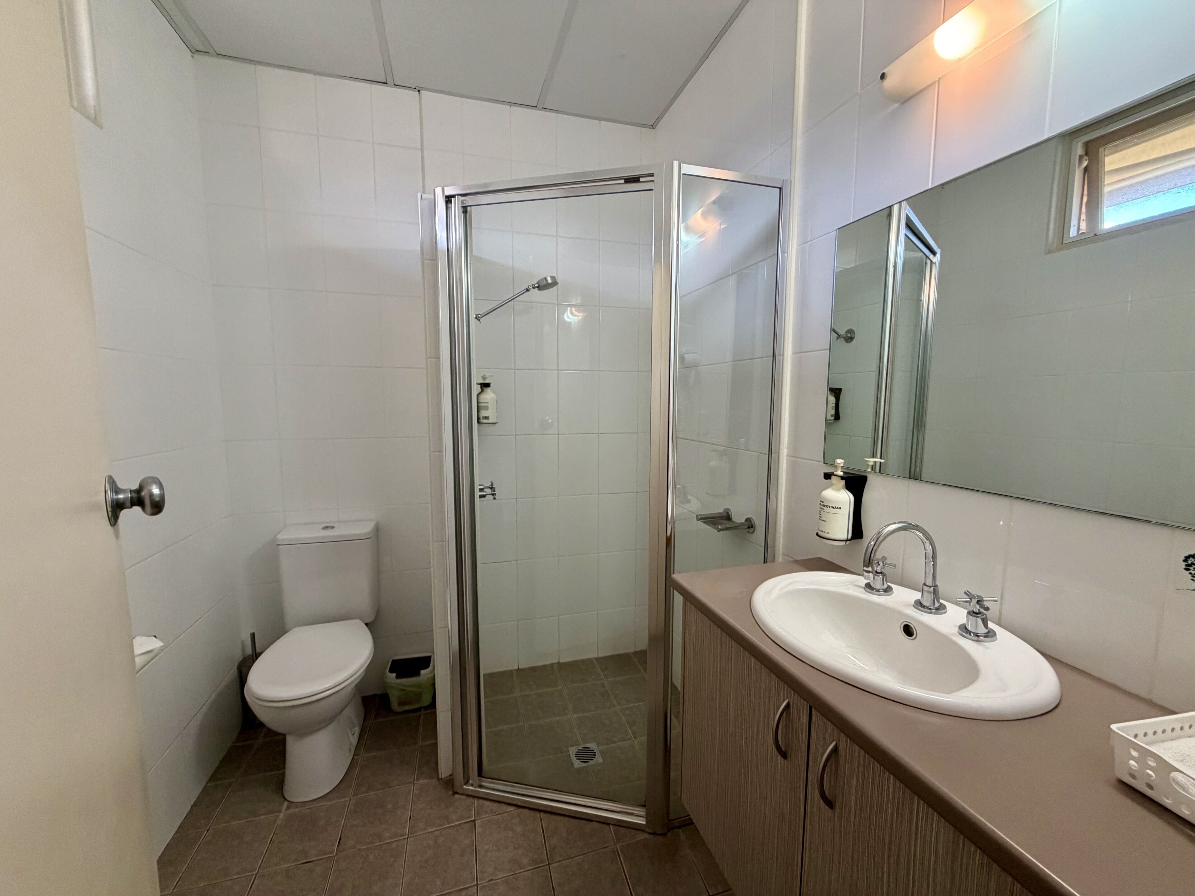 Une salle de bain comprenant des toilettes, une douche fermée par une paroi de verre, un lavabo avec un miroir et un meuble de rangement.