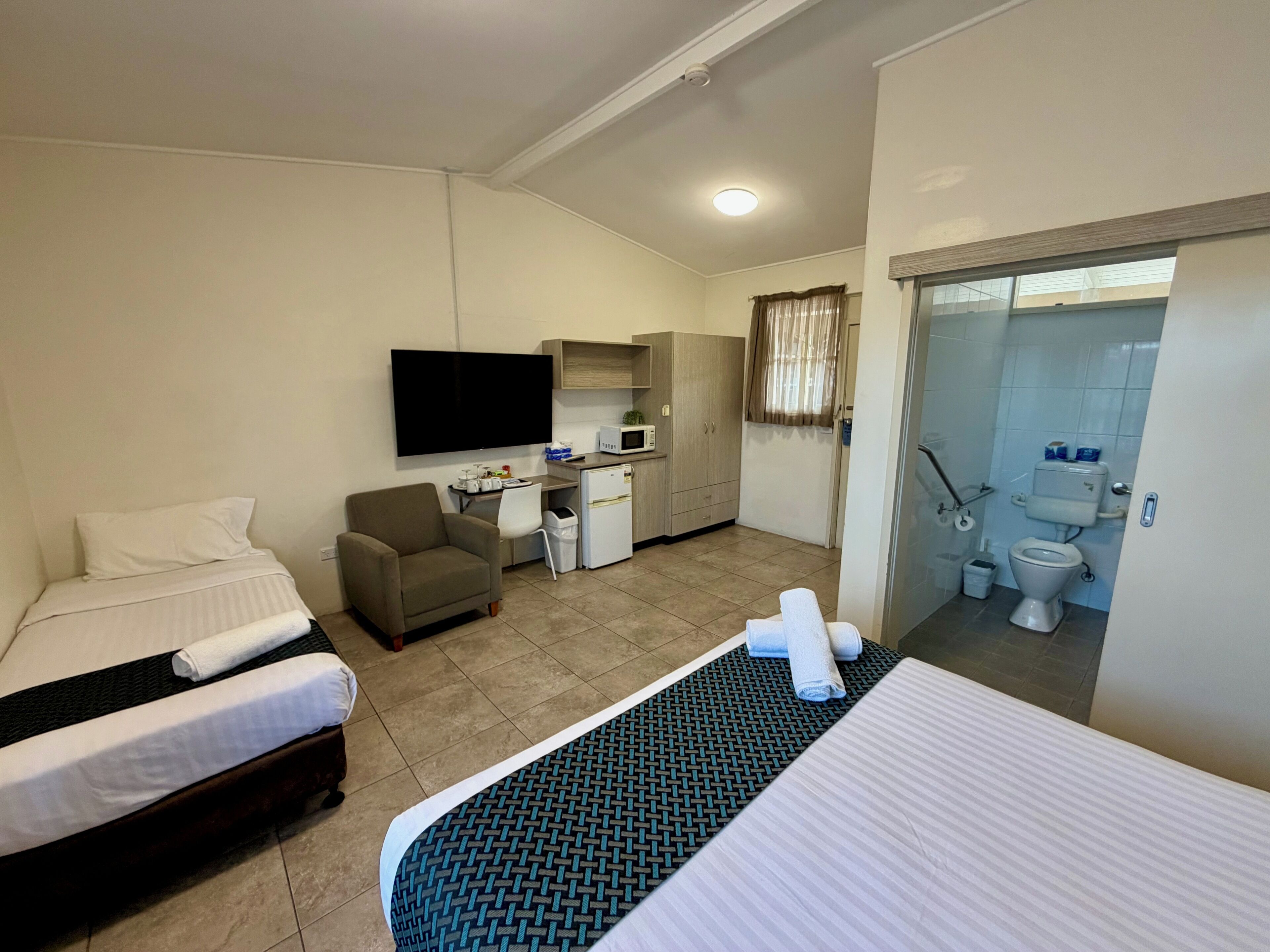 Une chambre d’hôtel avec deux lits, un bureau, une chaise, une télévision, un coin cuisine et une salle de bain.