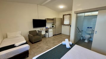 A hotel room with two beds, a desk, a chair, a TV, a kitchenette, and a bathroom.