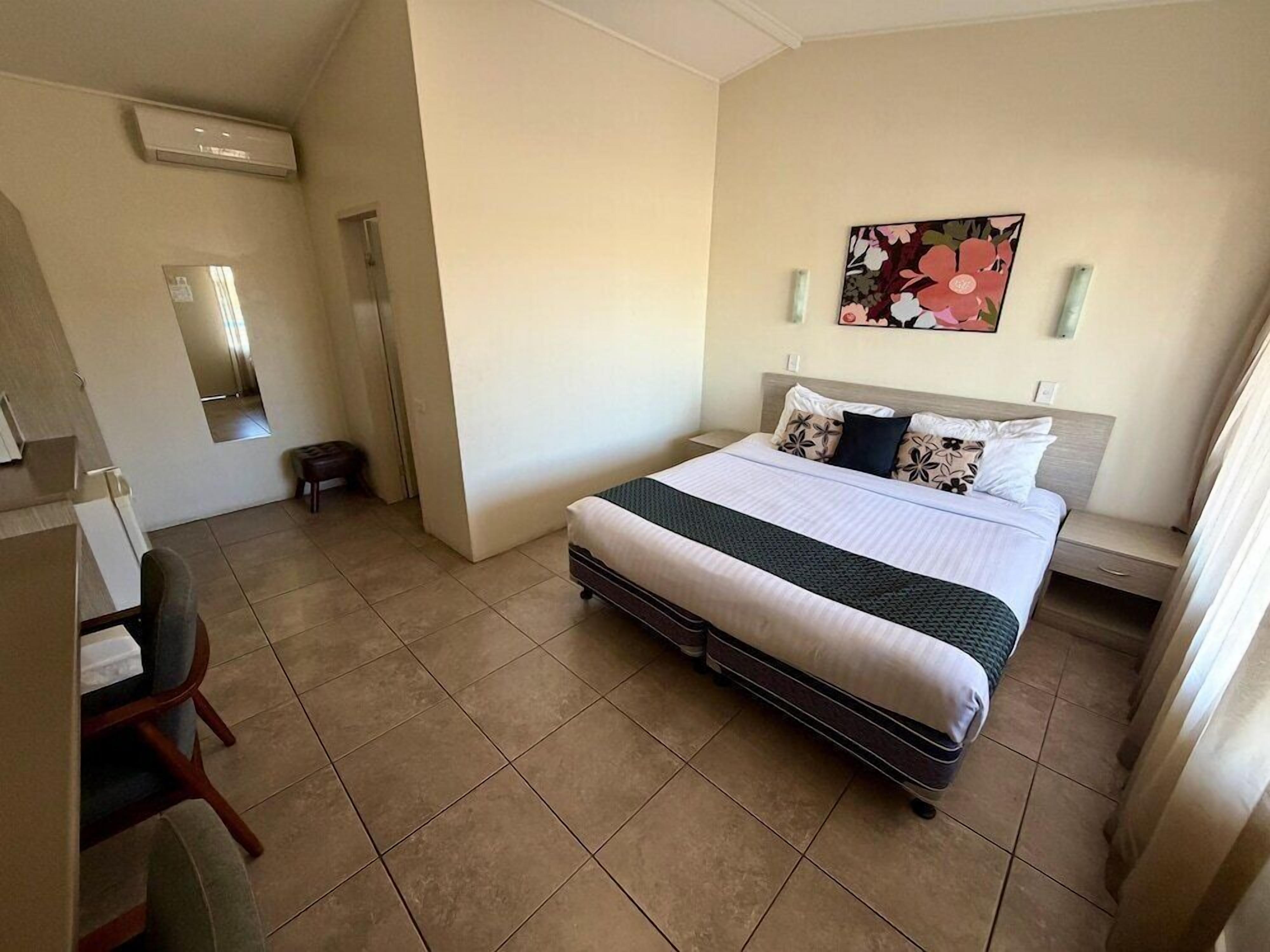 A bedroom with a bed, a chair, a desk, and a mirror.