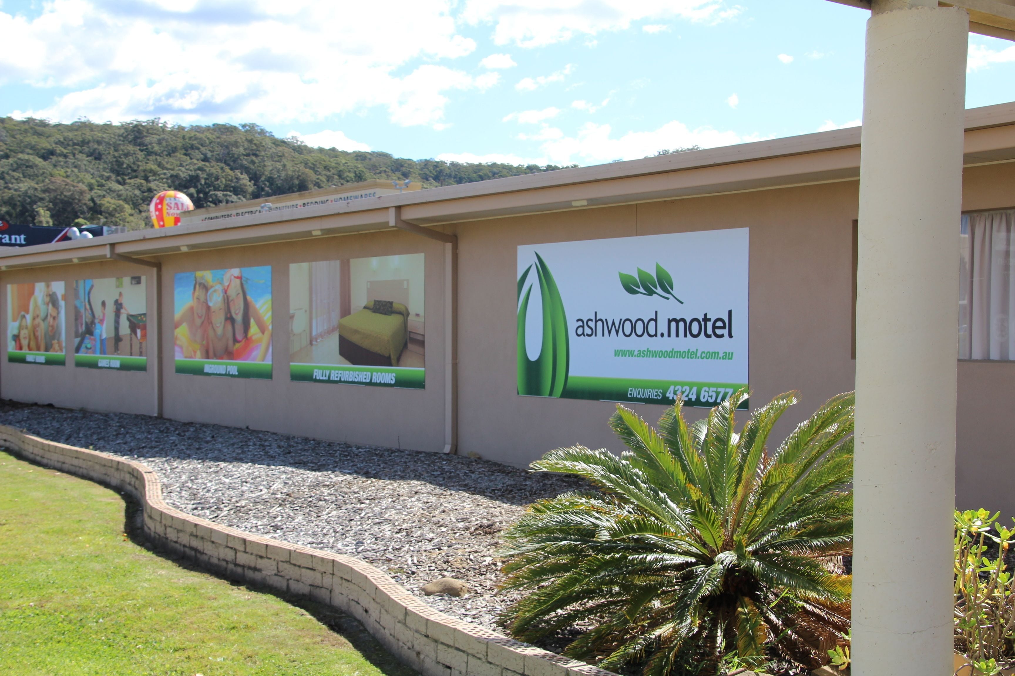 Un motel avec une enseigne publicitaire indiquant « ashwood.motel » et « chambres meublées avec des fruits ».