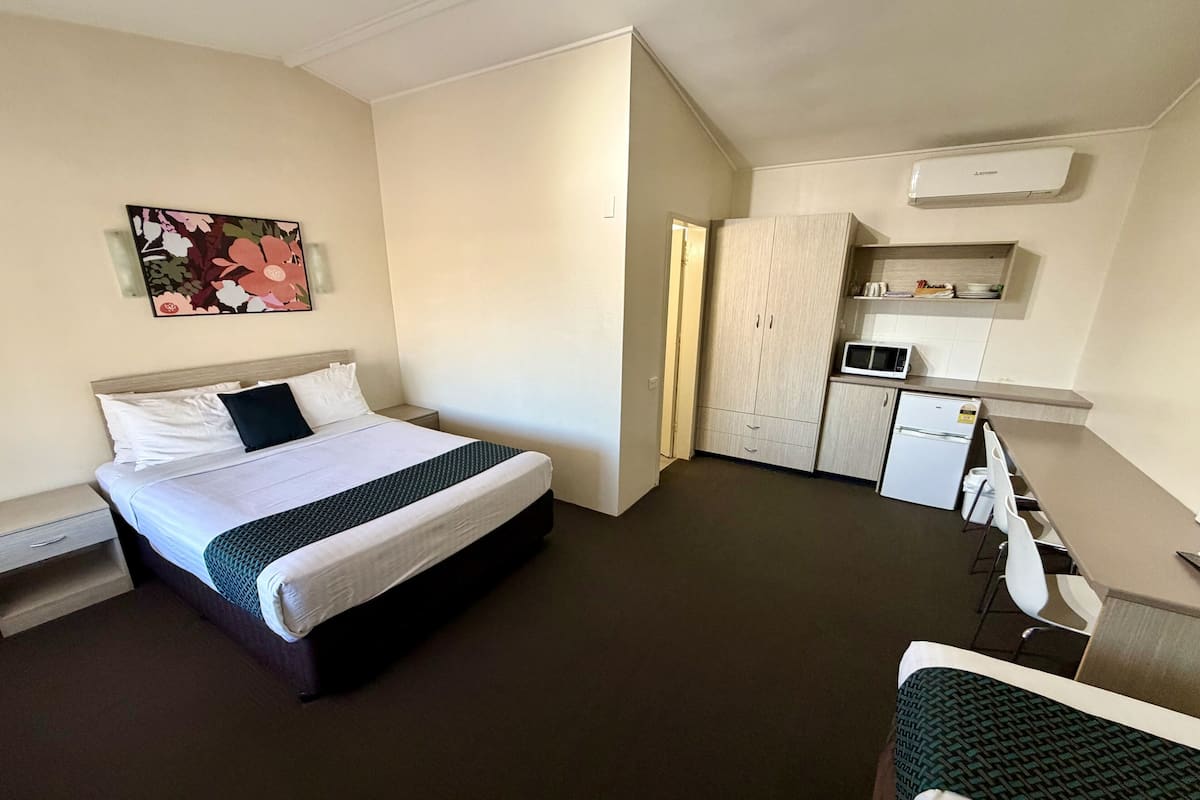 Habitación de hotel con cama, mesita de noche, un pequeño escritorio con silla, kitchenette y microondas.