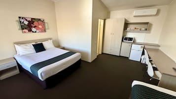 A hotel room with a bed, bedside table, a small desk with a chair, a kitchenette, and a microwave.