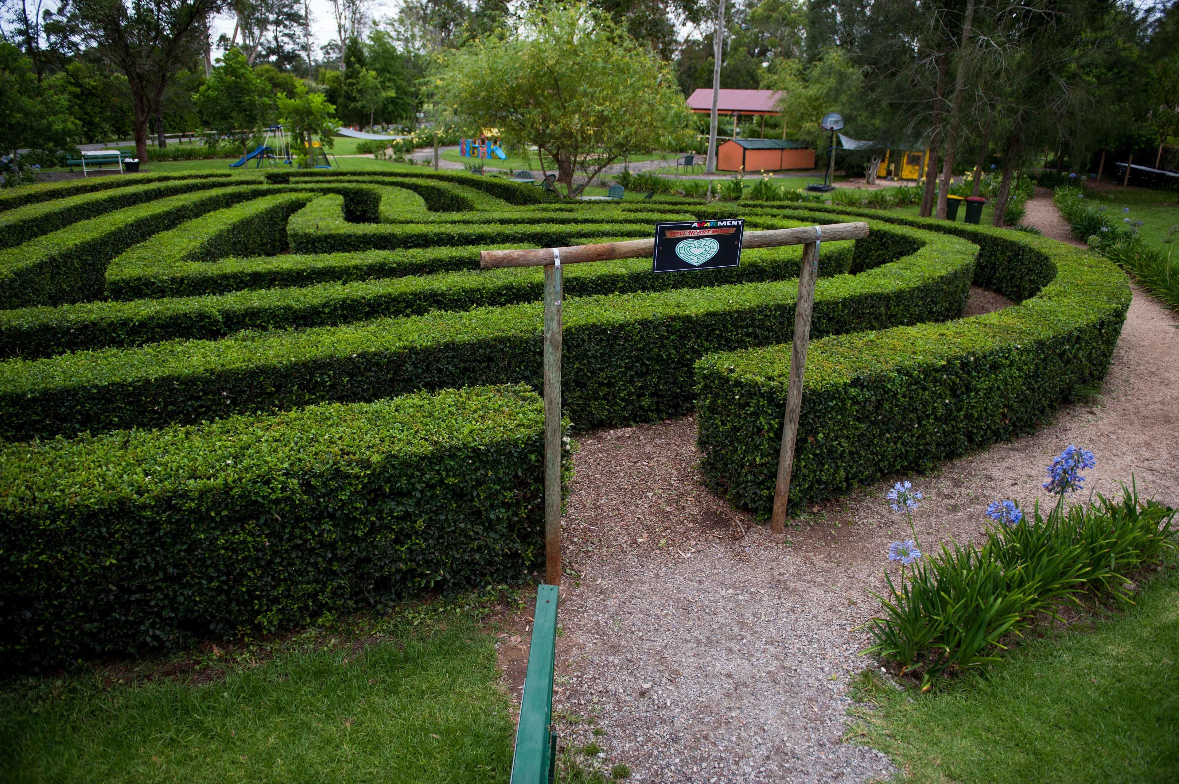 A landscaped garden with a maze-like hedge design, a wooden signpost, and a gravel path.
