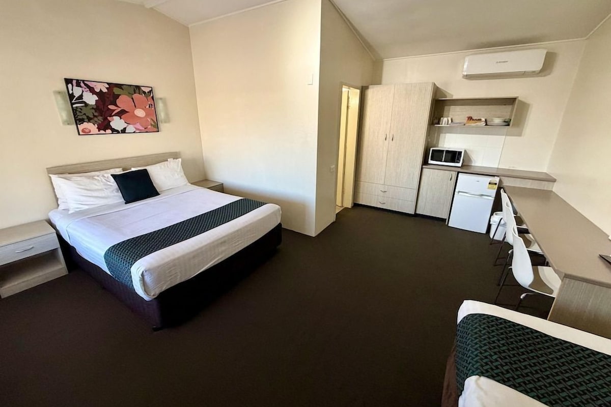 Ein Hotelzimmer mit Bett, Schreibtisch, Stuhl, Mikrowelle und Kleiderschrank.
