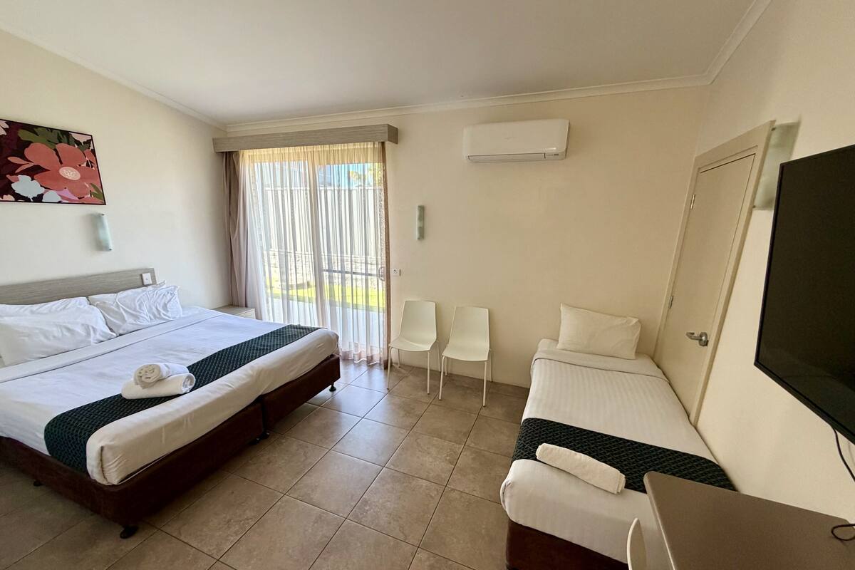 Una habitación de hotel con cama, sofá, televisión y ventana con cortinas.