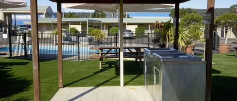 A covered outdoor seating area with a pool in the background.