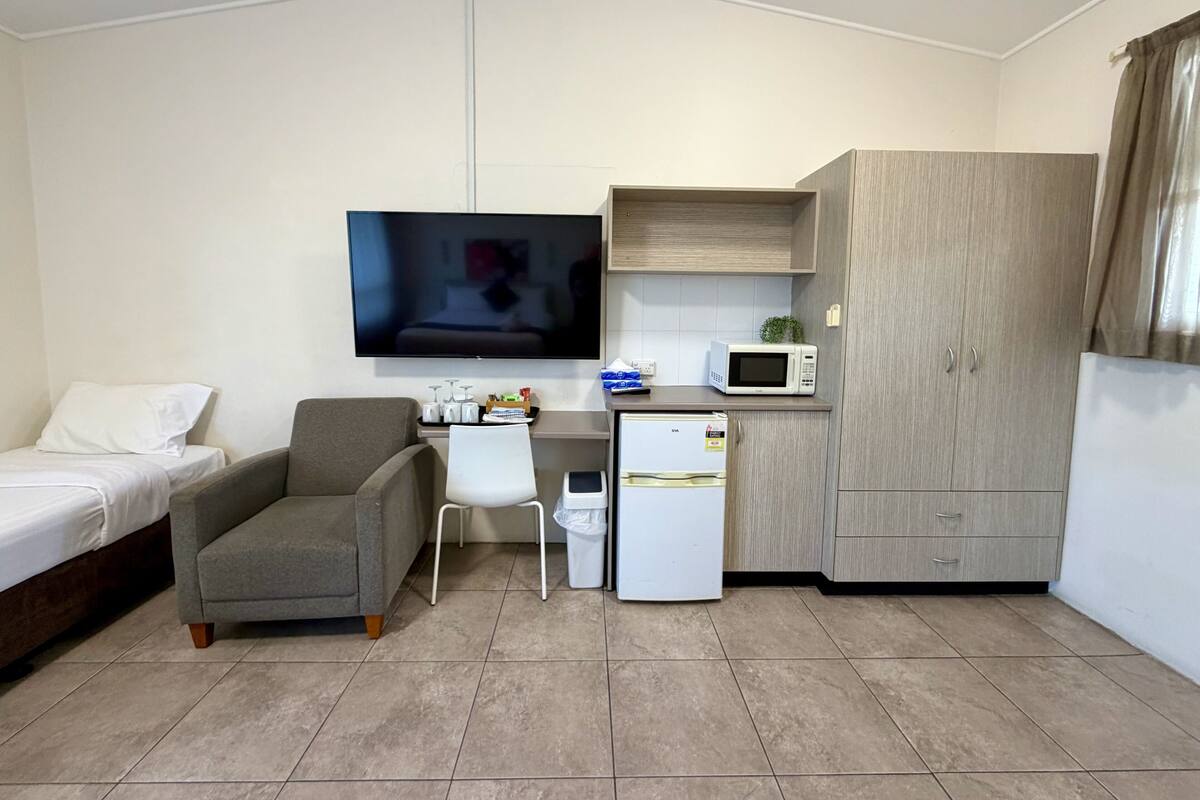 Habitación de hotel compacta con cama, sofá, escritorio con microondas, refrigerador y televisor montado en la pared.