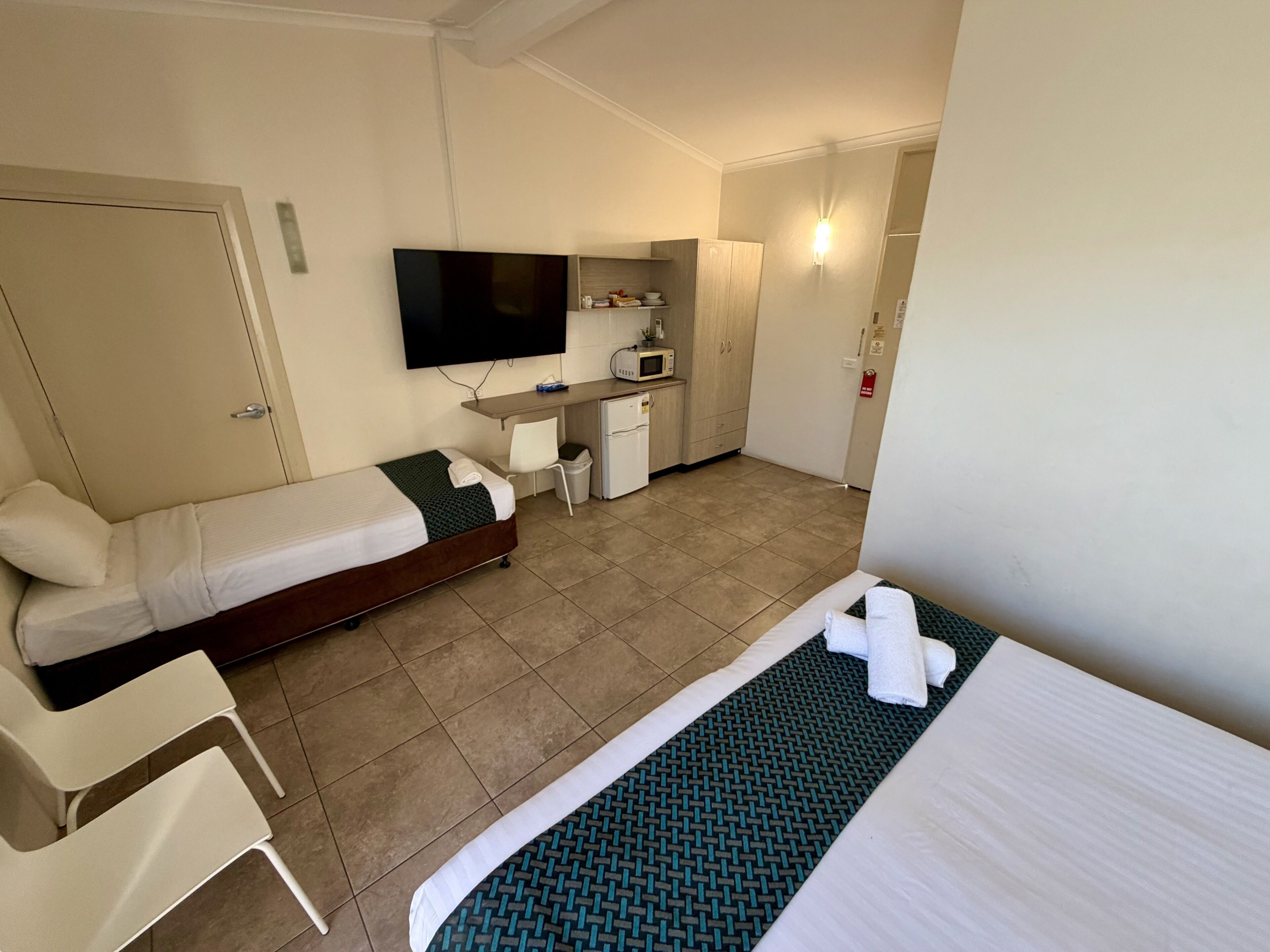 A hotel room with a bed, a desk, a television, a microwave, and a small kitchenette.