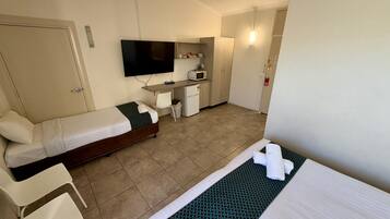 A hotel room with a bed, a desk, a television, a microwave, and a small kitchenette.