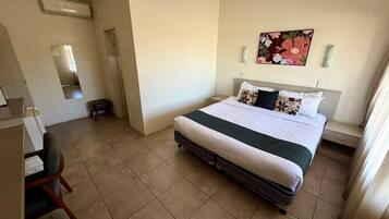 A hotel room with a bed, bedside tables, a chair, a mirror, and a wall-mounted artwork.