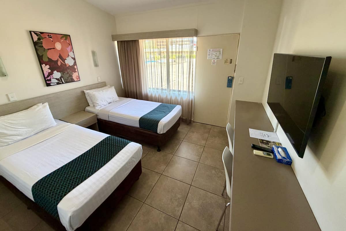 Habitación de hotel con dos camas, televisión y ventana con cortinas.
