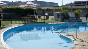 Uma piscina com uma escada de metal, cercada por uma grade, e um edifício com uma placa ao fundo.