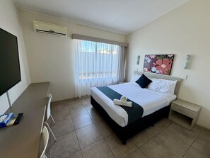 Habitació d'hotel amb llit, escriptori, cadira, televisió, aire condicionat, finestra amb cortines, taulell de nit, calaix i un quadre a la paret.